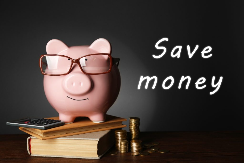 Piggy bank with glasses, coins and books on table, gray background.